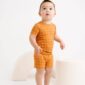 Child in orange plaid outfit standing indoors.