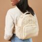 Woman wearing beige quilted backpack, brown background.