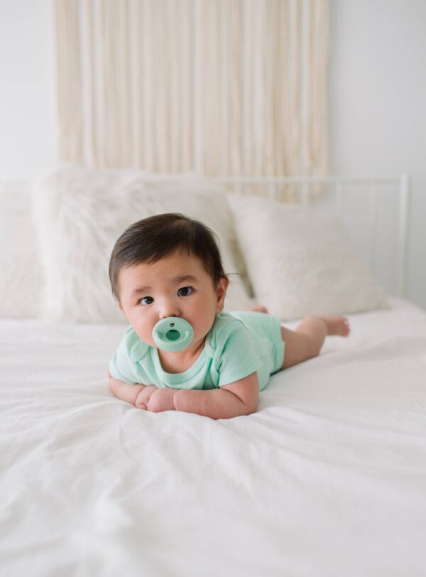itzy ritzy sweetie soother™ pacifier sets (2 pack): agave + succulent cables Baby with pacifier lying on bed
