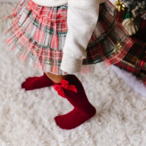 Child in plaid skirt and red socks by tree.