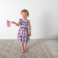 Smiling child holding American flag indoors.