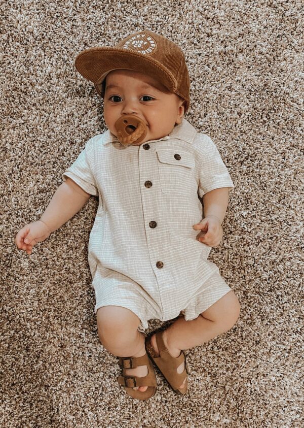 itzy ritzy sweetie soother™ pacifier sets (2 pack): agave + succulent cables Baby in romper and cap lying on carpet.