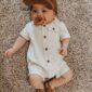 Baby in romper and cap lying on carpet.