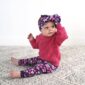 Baby in pink outfit with floral headband sitting.