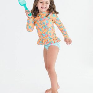 Girl in floral swimsuit holding blue shovel, smiling.