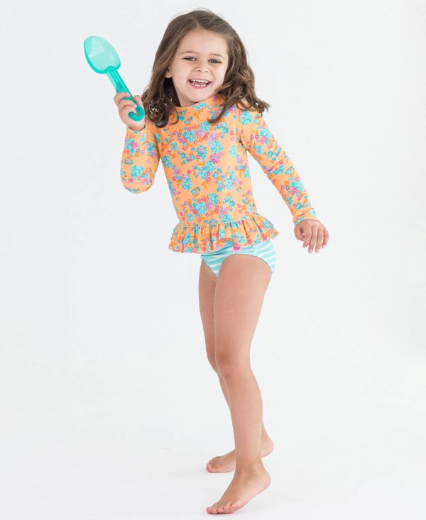 Girl in floral swimsuit holding blue shovel, smiling.