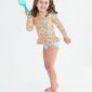 Girl in floral swimsuit holding blue shovel, smiling.
