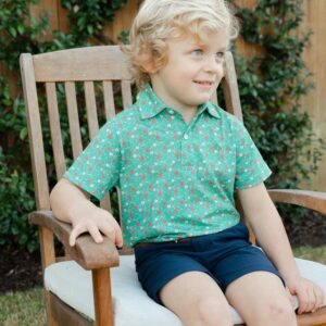 Child sitting on wooden chair outside smiling.
