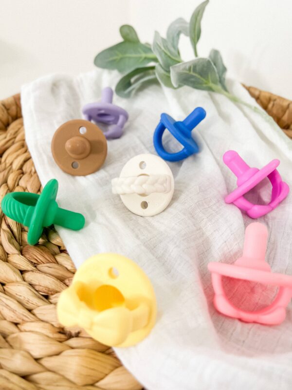 itzy ritzy sweetie soother™ pacifier sets (2 pack): agave + succulent cables Colorful baby pacifiers on a woven basket.