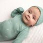 Smiling baby in green outfit on blanket.