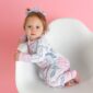 Baby in pajamas sitting on white chair, pink background.