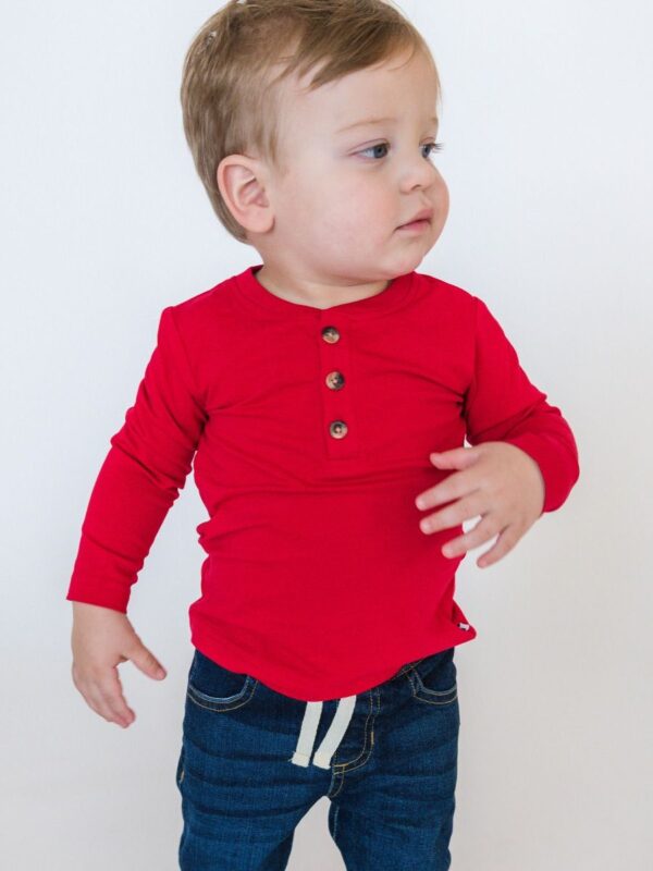 ruggedbutts red long sleeve henley t shirt Toddler in red shirt and jeans looking sideways.
