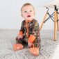 Baby in camo onesie sitting on carpet.
