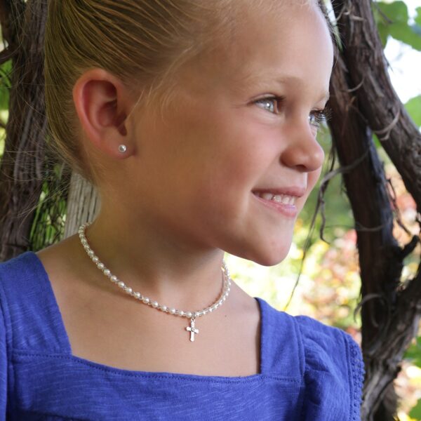 Girl smiling, wearing a pearl necklace outdoors.