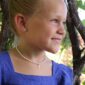 Girl smiling, wearing a pearl necklace outdoors.