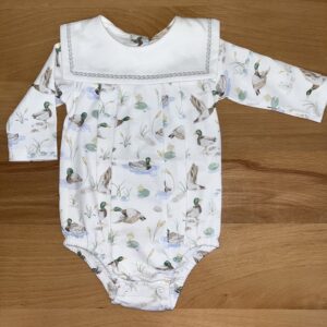 White baby onesie with duck pattern on wooden background.