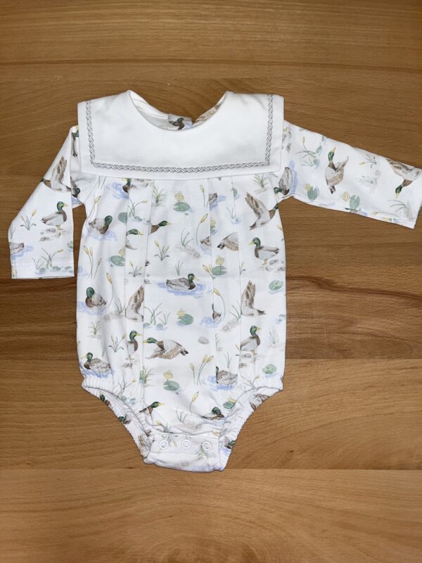 White baby onesie with duck pattern on wooden background.
