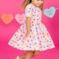 Child in dress with heart pattern, pink background.