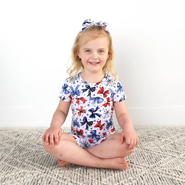 gigi and max eleanor bow clip bow 4th of july hair accessory Child in butterfly outfit sitting on rug, smiling.
