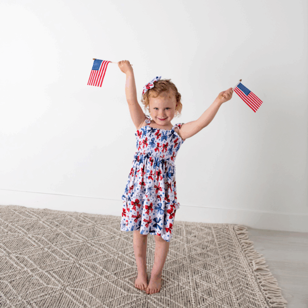 gigi and max eleanor bow clip bow 4th of july hair accessory Child holding American flags, wearing patriotic dress.