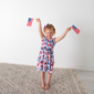 Child holding American flags, wearing patriotic dress.