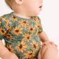 Baby in sunflower-patterned outfit sitting sideways.