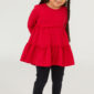 Child in red dress and black leggings smiling.