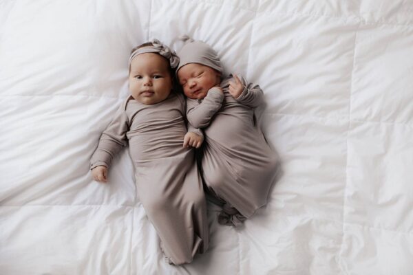 three little tots harbor mist taupe knotted gown Adorable newborn twins in matching outfits on bed.