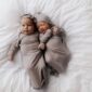 Adorable newborn twins in matching outfits on bed.
