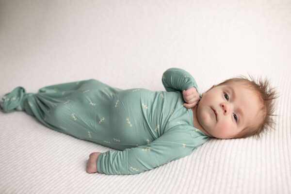 three little tots arrow print knotted newborn baby gown pajamas Baby in green onesie lying on blanket.