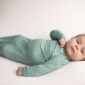 Baby in green onesie lying on blanket.