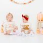 Two babies in pumpkin-themed outfits and decorations.