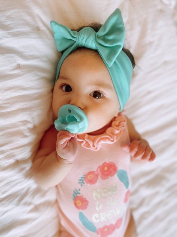 itzy ritzy sweetie soother™ pacifier sets (2 pack): agave + succulent cables Baby with turquoise headband and pacifier smiling.
