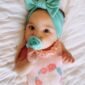 Baby with turquoise headband and pacifier smiling.