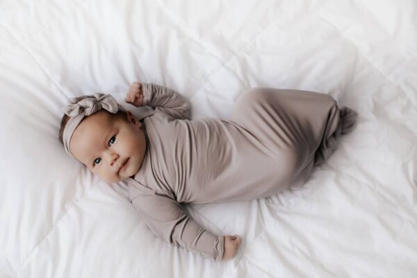 three little tots harbor mist taupe knotted gown Baby in taupe wrap lying on white bedding.