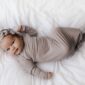 Baby in taupe wrap lying on white bedding.