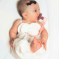 Baby with pacifier laying on white blanket.