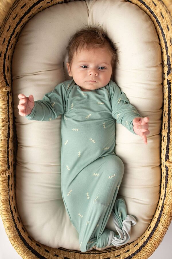three little tots arrow print knotted newborn baby gown pajamas Baby in teal onesie lying in a basket.