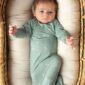 Baby in teal onesie lying in a basket.