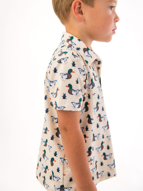 ruggedbutts mallard marsh active polo Child wearing duck-patterned shirt, side profile view.