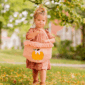 Child holding pumpkin basket in autumn leaves.
