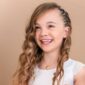 Smiling girl with curly hair wearing a necklace.