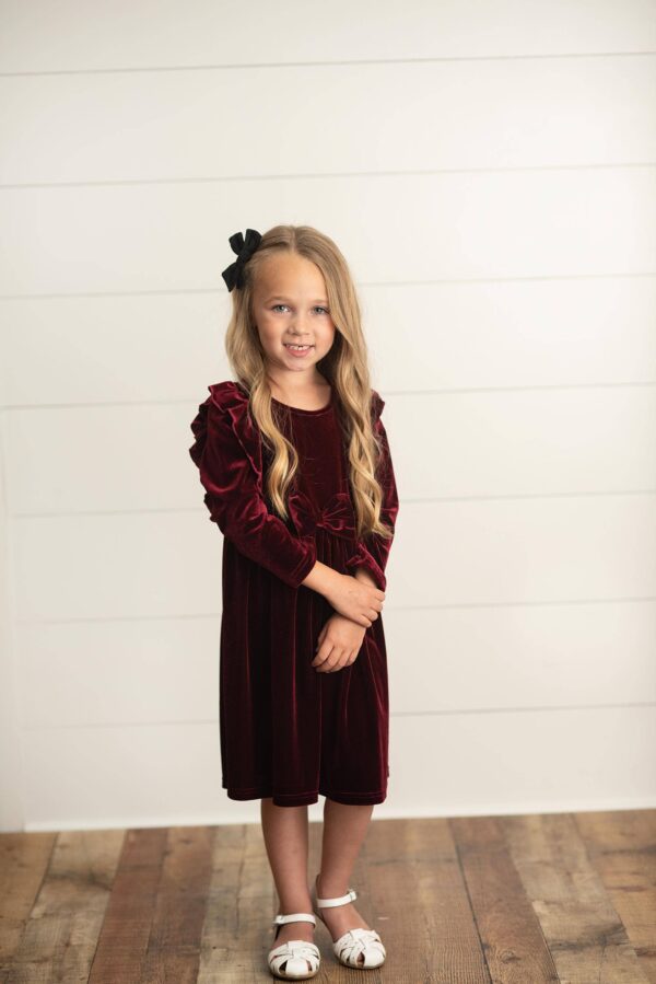 oopsie daisy kids burgundy wine velvet bow ruffle holiday party dress Young girl in burgundy dress smiling indoors.