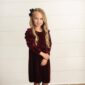 Young girl in burgundy dress smiling indoors.
