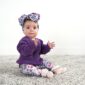 Baby in purple sweater and floral headband sitting.