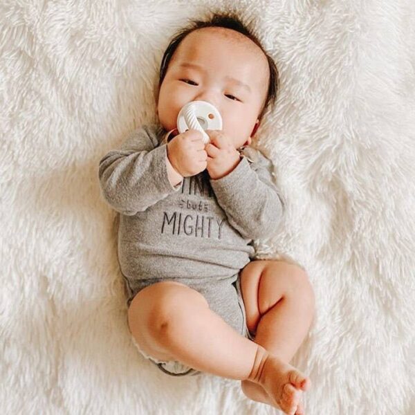 itzy ritzy sweetie soother™ pacifier sets (2 pack): agave + succulent cables Baby in gray onesie with pacifier on fluffy blanket.