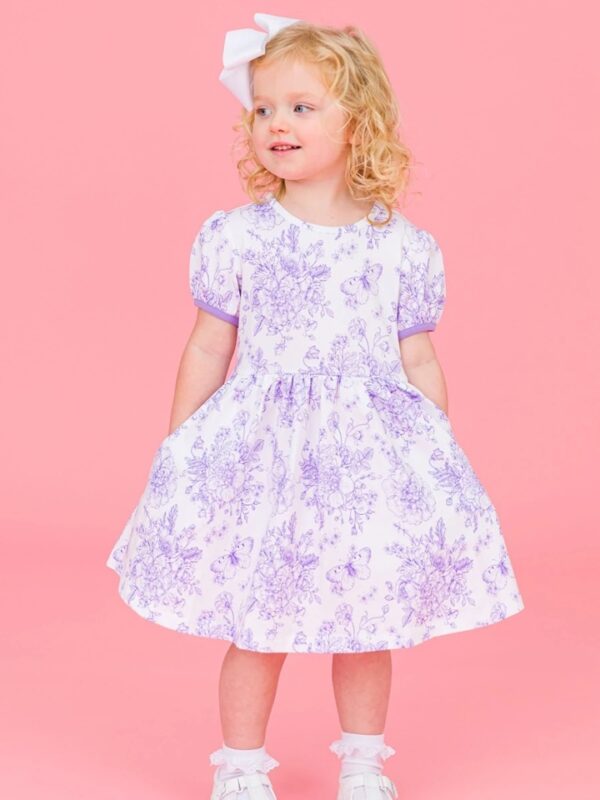 Child in floral dress and white bow smiling.