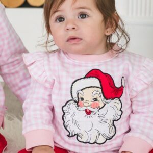 Child in Santa-themed pajamas sitting indoors.