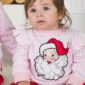 Child in Santa-themed pajamas sitting indoors.