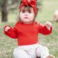 Baby in red outfit sitting on grass